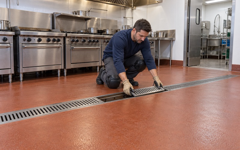 A stainless trench drain grate lowered back into a coved urethane cement floor in a Buffalo Grove restaurant kitchen.